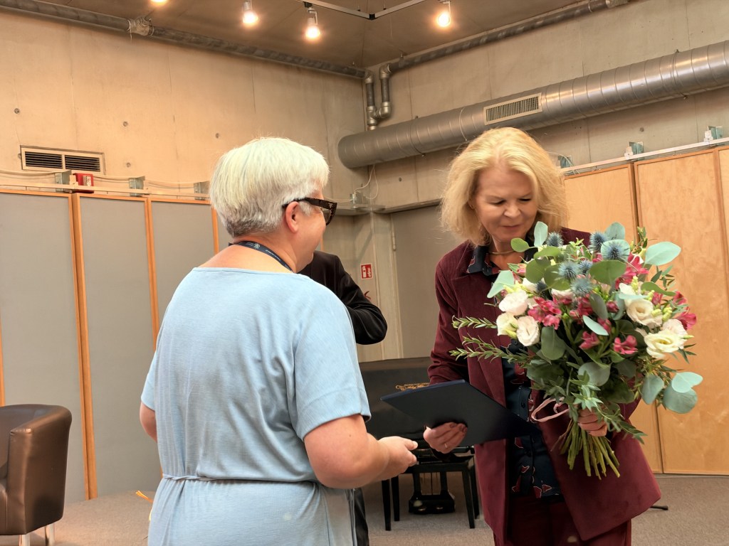 Osoba wręczająca bukiet kwiatów kobiecie podczas wydarzenia.