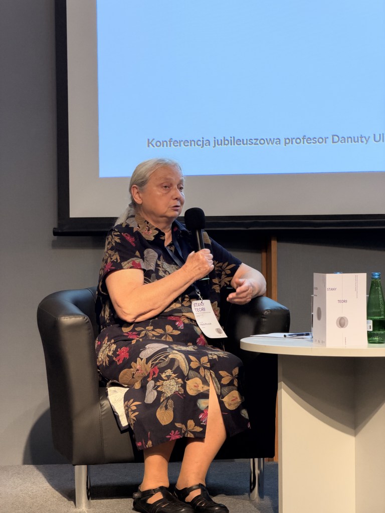 Profesor omawia temat konferencji jubileuszowej na temat teorii, siedząc na panelu dyskusyjnym.